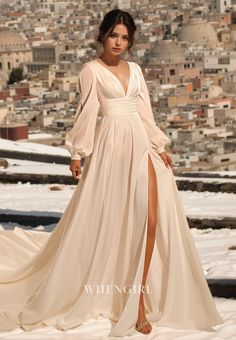 a woman in a long white dress standing on snow covered ground with buildings behind her