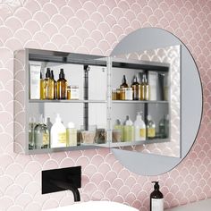 a bathroom with pink and white wallpaper, a round mirror and various bottles on the shelf