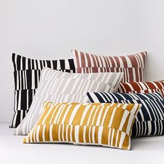 four pillows are lined up against a white wall, each with different colors and patterns