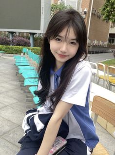 a young woman sitting on top of a wooden bench next to a blue and white chair