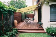 a wooden deck surrounded by greenery and potted plants with an awning over it