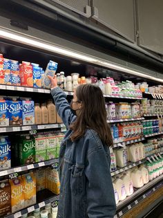 a woman is shopping for milk in a grocery store with her hand up to the sky