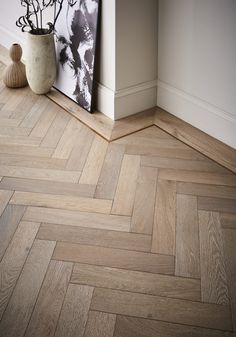 a vase with flowers on the floor next to a wooden herringbone pattern wallpaper