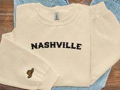 This Nashville embroidered crewneck sweatshirt is the perfect blend of style and comfort! Whether you're out and about or cuddled up at home, our crewnecks feature minimalistic designs that can be paired with any outfit. The surprise sleeve design perfectly complements the front, offering a whimsical touch that will make you smile throughout the day! Product Details:  * 50% cotton, 50% polyester * Pre-shrunk * Classic fit * 1x1 athletic rib knit collar with spandex * Air-jet spun yarn with a sof Custom Embroidered Fleece Crew Neck Top, Fleece Crew Neck Top With Custom Embroidery, Fan Apparel Crew Neck Sweatshirt With Embroidered Logo, Fan Apparel Sweatshirt With Embroidered Logo And Crew Neck, Fan Apparel Cotton Sweatshirt With Embroidered Graphics, Fan Apparel Sweatshirt With Embroidered Logo, Fall T-shirt With Embroidered Logo In Relaxed Fit, Relaxed Fit T-shirt With Embroidered Logo For Fall, Fall Relaxed Fit T-shirt With Embroidered Logo