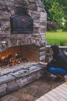 a woman kneeling down in front of an outdoor fireplace