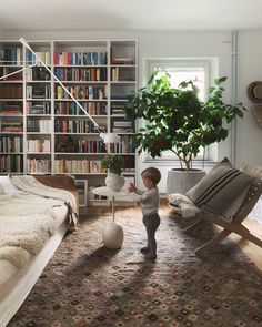 a young boy standing in front of a book shelf next to a bed and chair