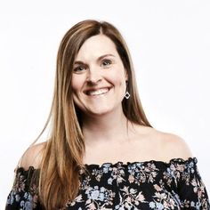 a woman with long hair smiling and wearing an off the shoulder floral top in front of a white background