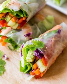 two rolls filled with vegetables and lettuce on top of a wooden cutting board