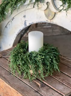 a white candle sitting on top of a wooden table next to a planter filled with greenery