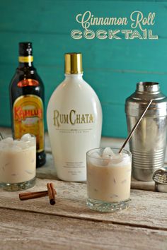 two glasses filled with rumchata and cinnamon rolls next to bottles of alcohol on a wooden table