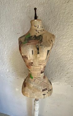 a mannequin made out of newspaper sitting on top of a white table next to a wall