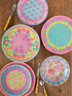 colorful plates and utensils laid out on a wooden table with flowers painted on them