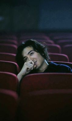 a man is sitting in the middle of a row of red seats with his hand on his chin