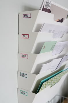 several file folders are stacked up on a white wall with labels attached to them