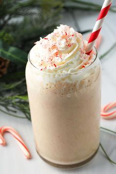 a drink with whipped cream and sprinkles in a glass next to candy canes