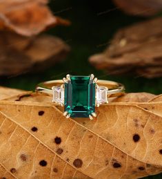 an emerald and diamond ring sitting on top of a leaf