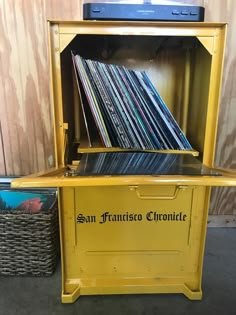 an old yellow record player with many records in it's storage compartment and wicker baskets next to it