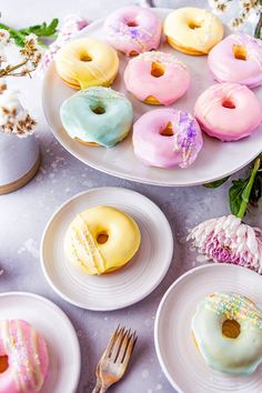 several donuts are on white plates with pink, blue and yellow frosting