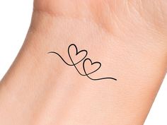 a small black heart tattoo on the left side of a woman's arm and wrist