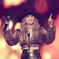 a woman wearing a black hat and holding a microphone in her right hand while standing on stage