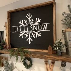 a wooden sign that says let it snow on top of a shelf next to potted plants