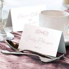 two place cards are sitting on a table with silverware and wine glasses in the background