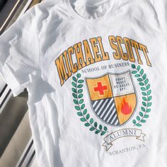 the michael scott school of business t - shirt is laying on top of a table