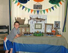 a young boy sitting at a table in front of a fish themed birthday party banner