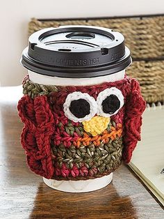 a coffee cup cozying with an owl face on the front and bottom, sitting next to a notebook