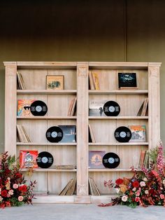 two wooden bookshelves with vinyl records on them and flowers in the foreground