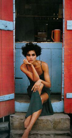 a woman sitting on steps in front of a red door with her hand under her chin