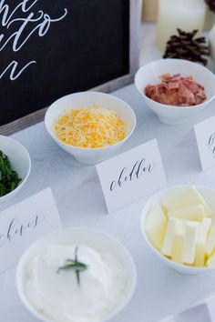 the table is set up with different types of cheeses and other foods in bowls