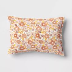 an orange and pink pillow with flowers on it, against a white wallpaper background