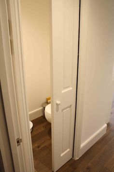 an open door leading to a bathroom with a toilet in the corner and wood flooring