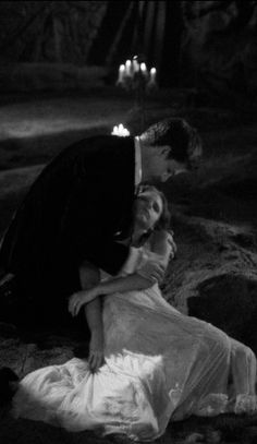 a man kneeling down next to a woman on top of a rocky hillside with candles in the background