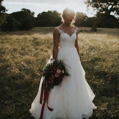 a woman in a wedding dress standing in the grass with her bouquet on her shoulder