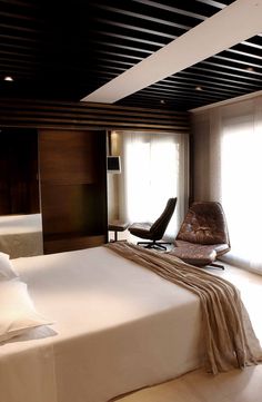 a bedroom with a bed, chair and window in the room that has wooden slats on the ceiling