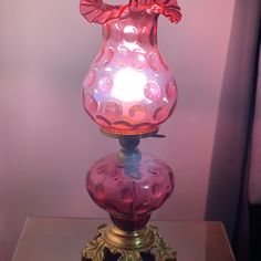 a pink glass vase sitting on top of a wooden table next to a light bulb