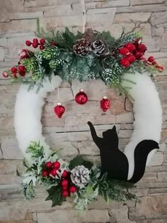 a christmas wreath with a black cat and pine cones hanging from it's side