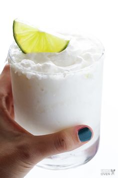 a hand holding a glass filled with whipped cream and a lime slice