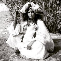 an old black and white photo of a woman sitting on the ground in front of trees