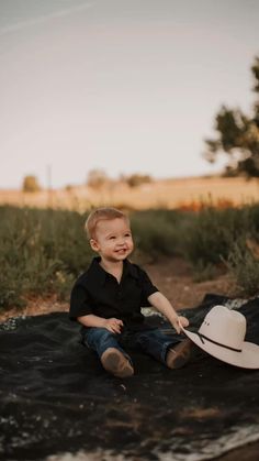 a little boy sitting on top of a blanket wearing a cowboy hat and smiling at the camera