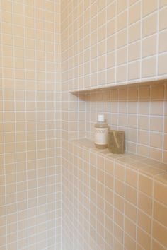 a white tiled bathroom with shelfs and soap dispenser on the wall