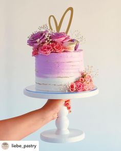 a hand holding a cake with flowers on it and the letter d is spelled in gold