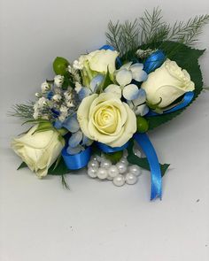 a bouquet of white roses and blue flowers with pearls on the side, sitting on a table