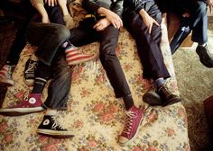 four young men sitting on top of a floral covered couch with their feet up in the air