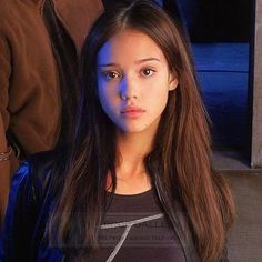 a girl with long hair standing in front of a building and looking at the camera