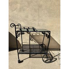 a wrought iron serving cart with glass top and wheels on the side of a building