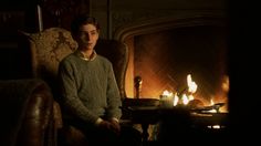 a young man sitting in front of a fire place with his feet on the chair