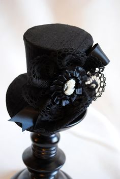 This victorian goth mini top hat is a simple yet elegant piece.It is covered with black silk shantung and adorned with black satin ribbon in a vertical half bow, vintage black cotton lace in a rosette, pleated satin ribbon, which forms an oval frame for a beautiful black and white victorian profile cameo. Choose between with or without black veil. Also available in a white and black combination: https://www.etsy.com/bizarrenoir/listing/166826619/gothic-mini-top-hat-in-purple-velvet?ref=shop_home Handmade Fitted High Crown Mini Hats, Handmade Fitted Mini Hat With High Crown, Gothic Black Brimmed Costume Hat, Gothic Top Hat With Short Brim For Halloween, Black Gothic Party Hat, Gothic Top Hat With High Crown For Parties, Gothic Black Mini Hats For Halloween, Black Gothic Mini Hats For Costume Party, Black Brimmed Mini Hats For Costumes